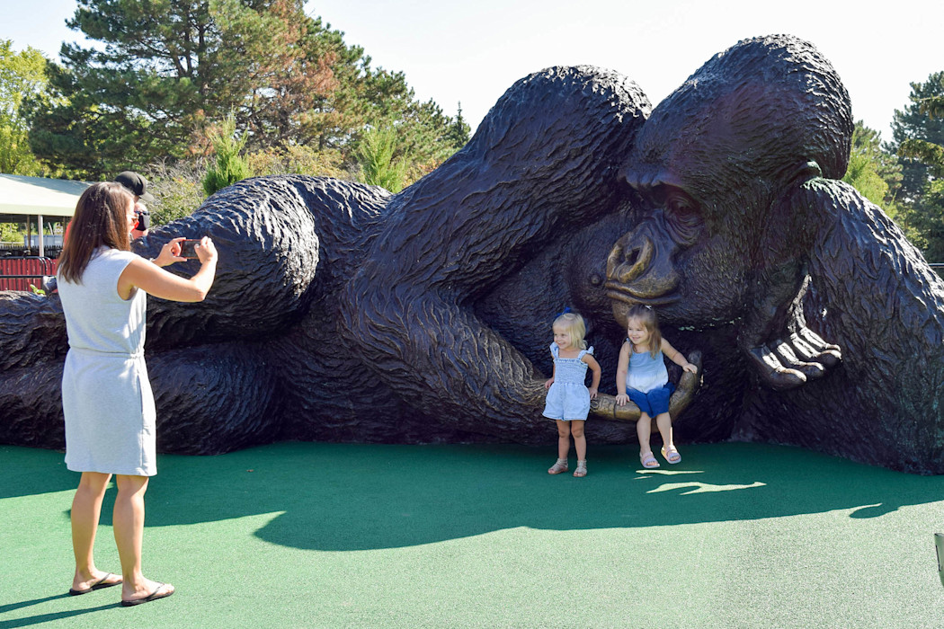 Two children pose in front of a large statue of a gorilla.