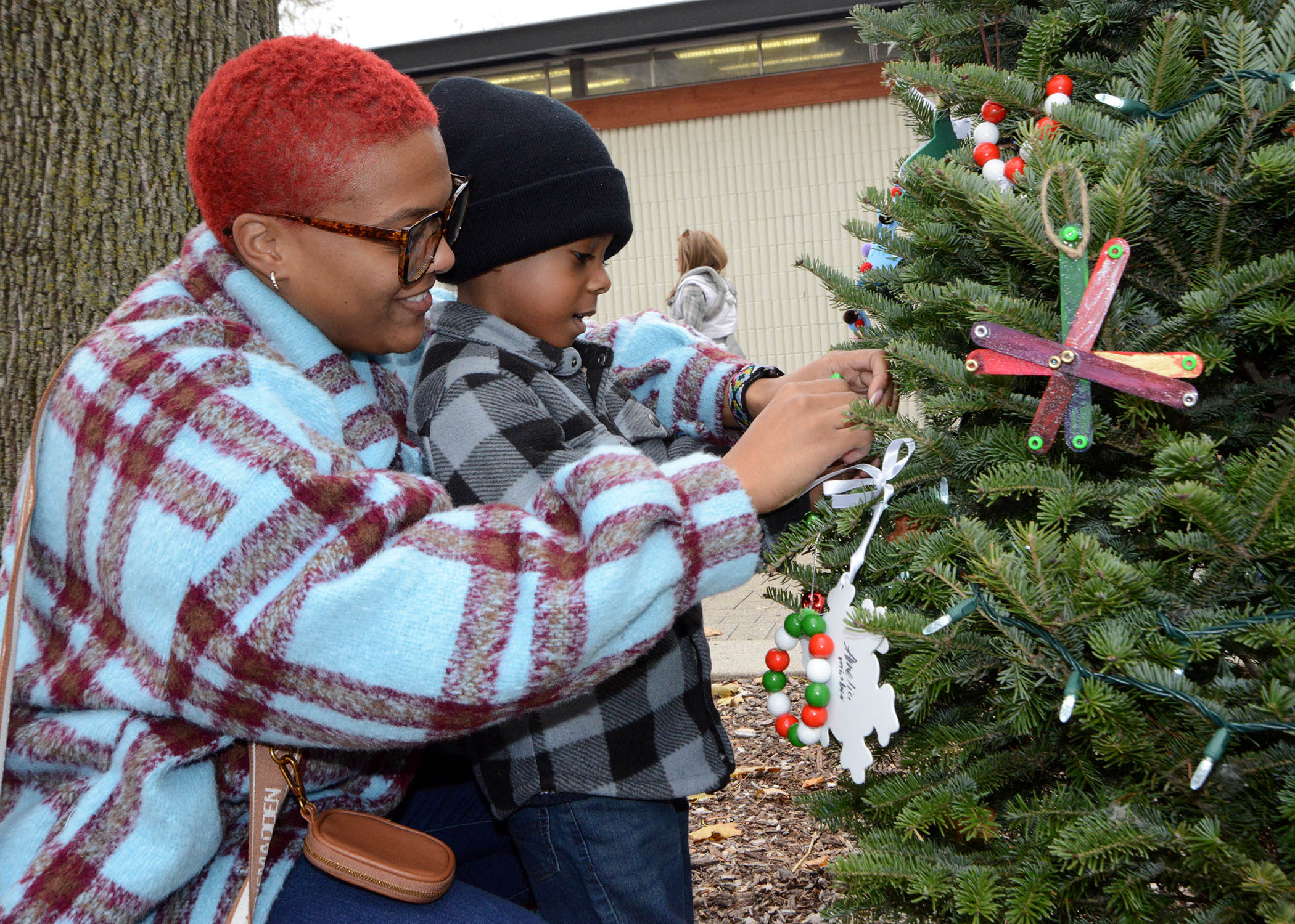 A mother and son decorate a Christmas tree with ornaments.