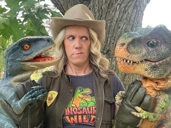 A woman stands between two dinosaur puppets. 