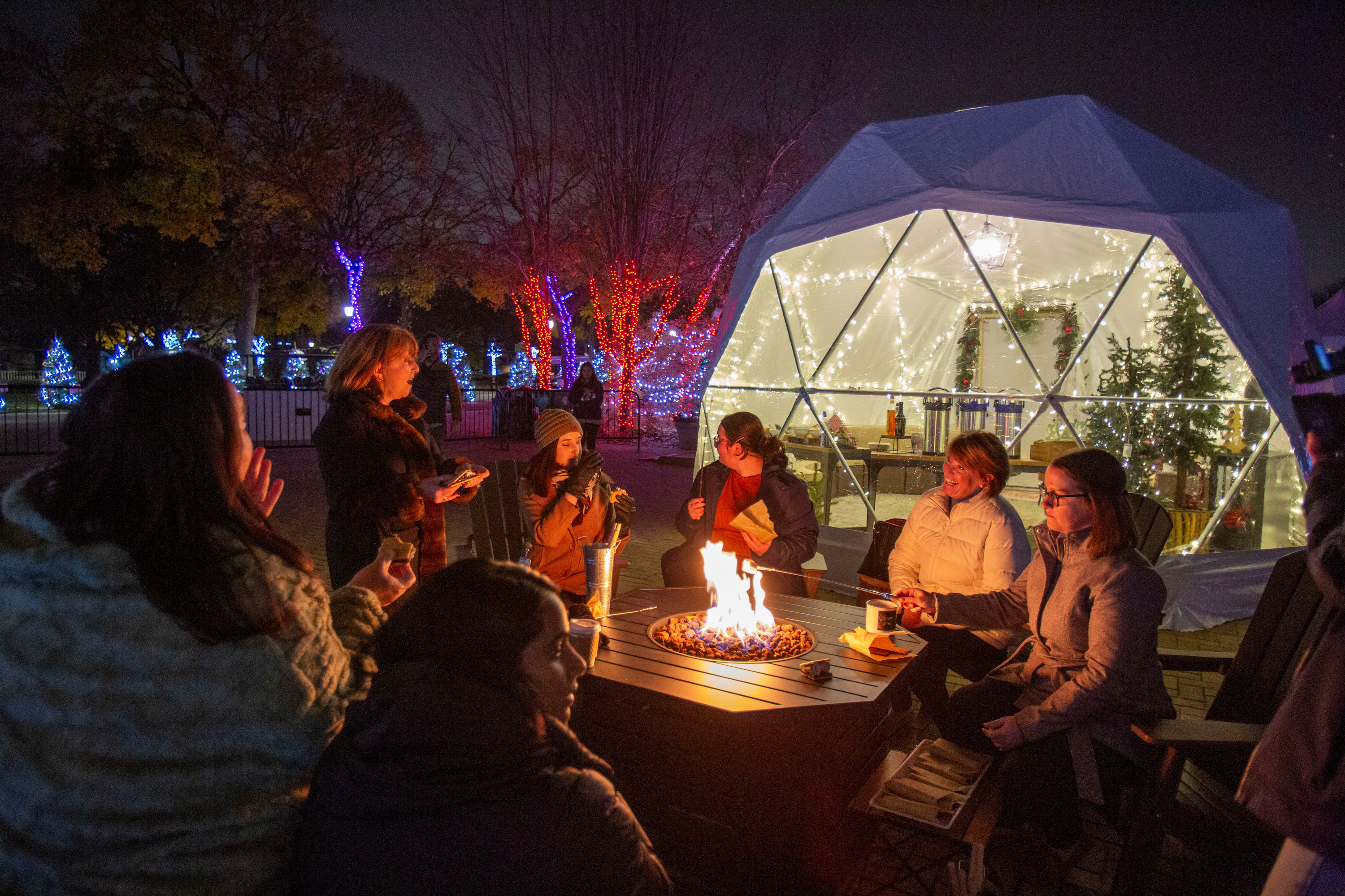 People gather around a fire pit in front of the holiday igloo.