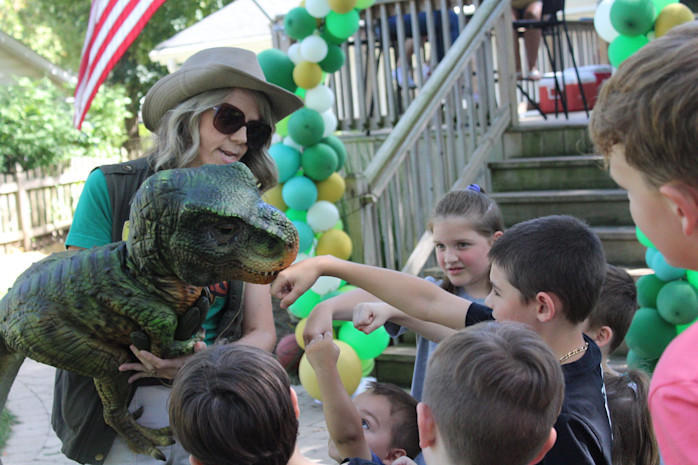 A woman in a ranger outfit holds a baby dinosaur puppet out to children. 