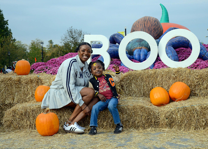 An adult and a child smile on hay bales in front of a sign that says Boo.