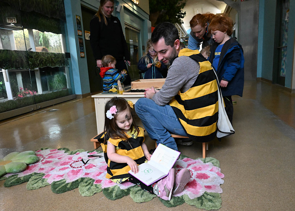A father and daughter read a book, dressed as bumblebees.