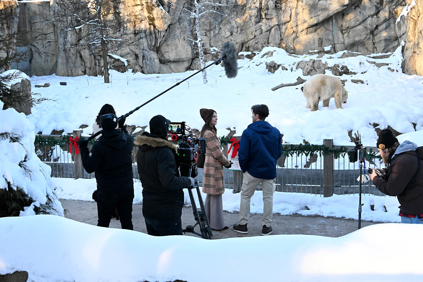 Two actors stand in front of a polar bear, being filmed by a professional movie crew. 