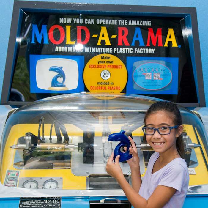 A child poses with a molded dolphin souvenir in front of a Mold-a-Rama machine at Brookfield Zoo Chicago.