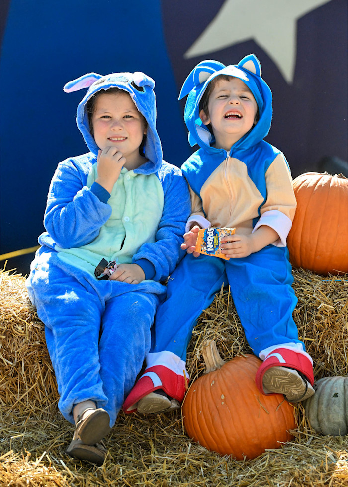 Children in costumes sit on a hay bale.