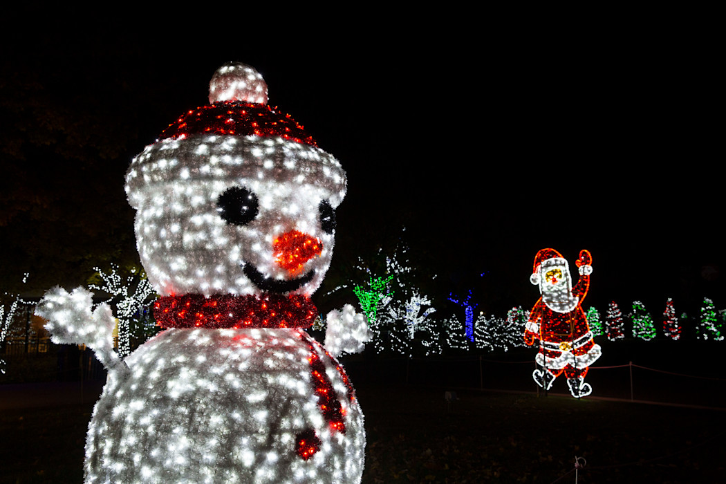 A snowman made of lights is standing in front of a santa made of light. 