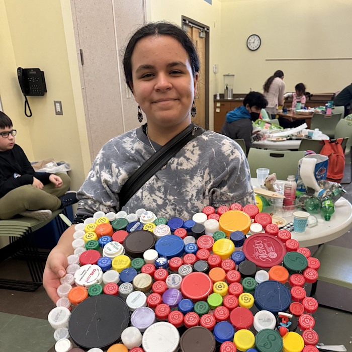 A middle-school aged student holds a box of plastic bottles. 