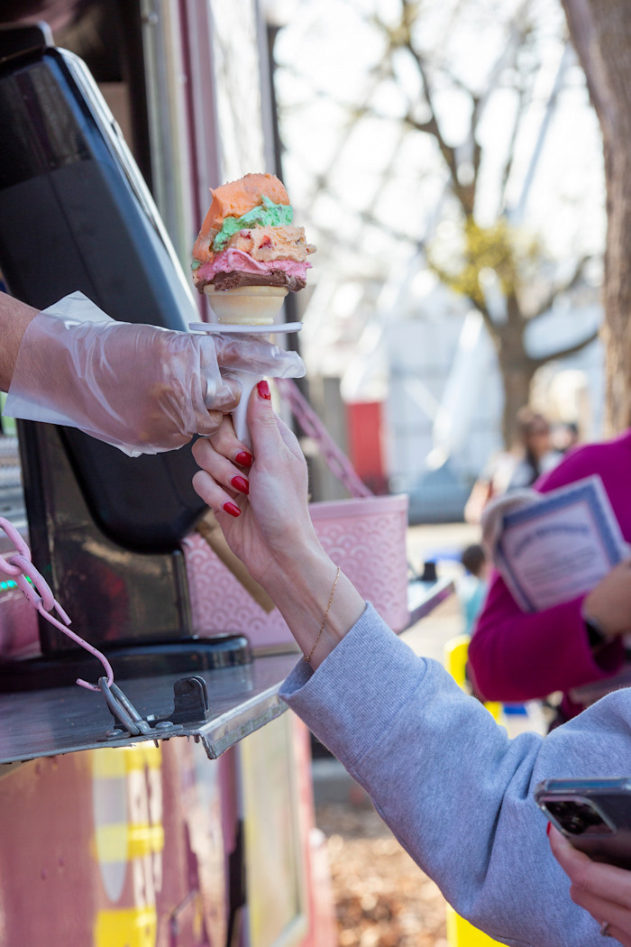 A hand reaches out of a window to hand an ice cream cone to a guest. 
