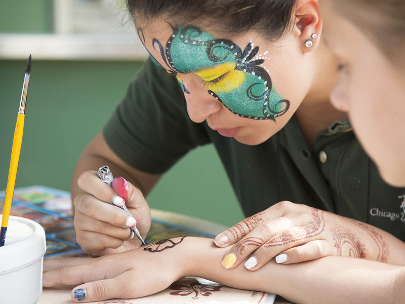 A photo of an artist giving a temporary henna tattoo to a young guest at Brookfield Zoo Chicago.